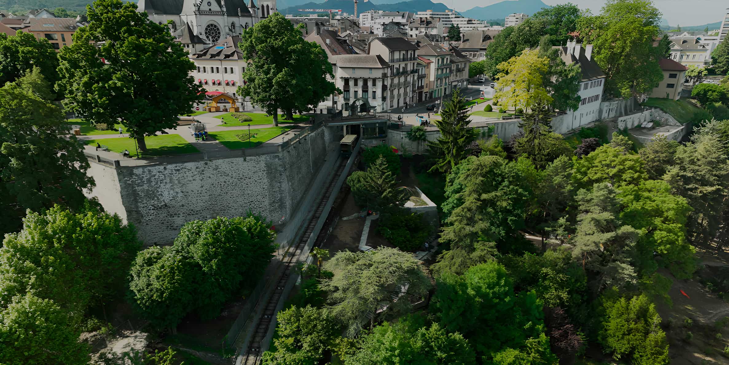 Aerial view of Annecy old town with a funicular railway cutting through lush green parkland and historic stone walls