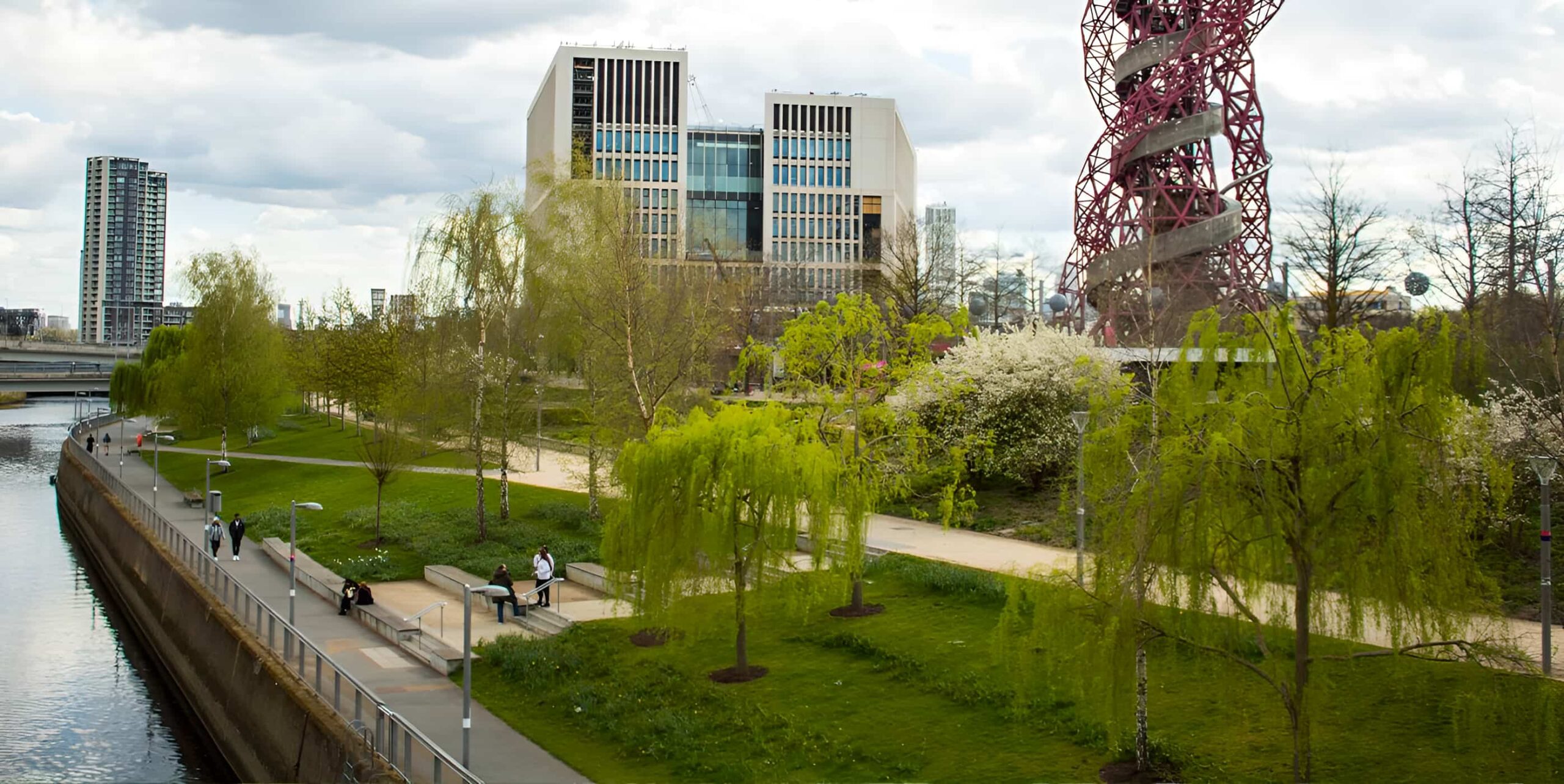 Queen Elizabeth Olympic Park with weeping willows, riverside path, ArcelorMittal Orbit tower and modern buildings in spring