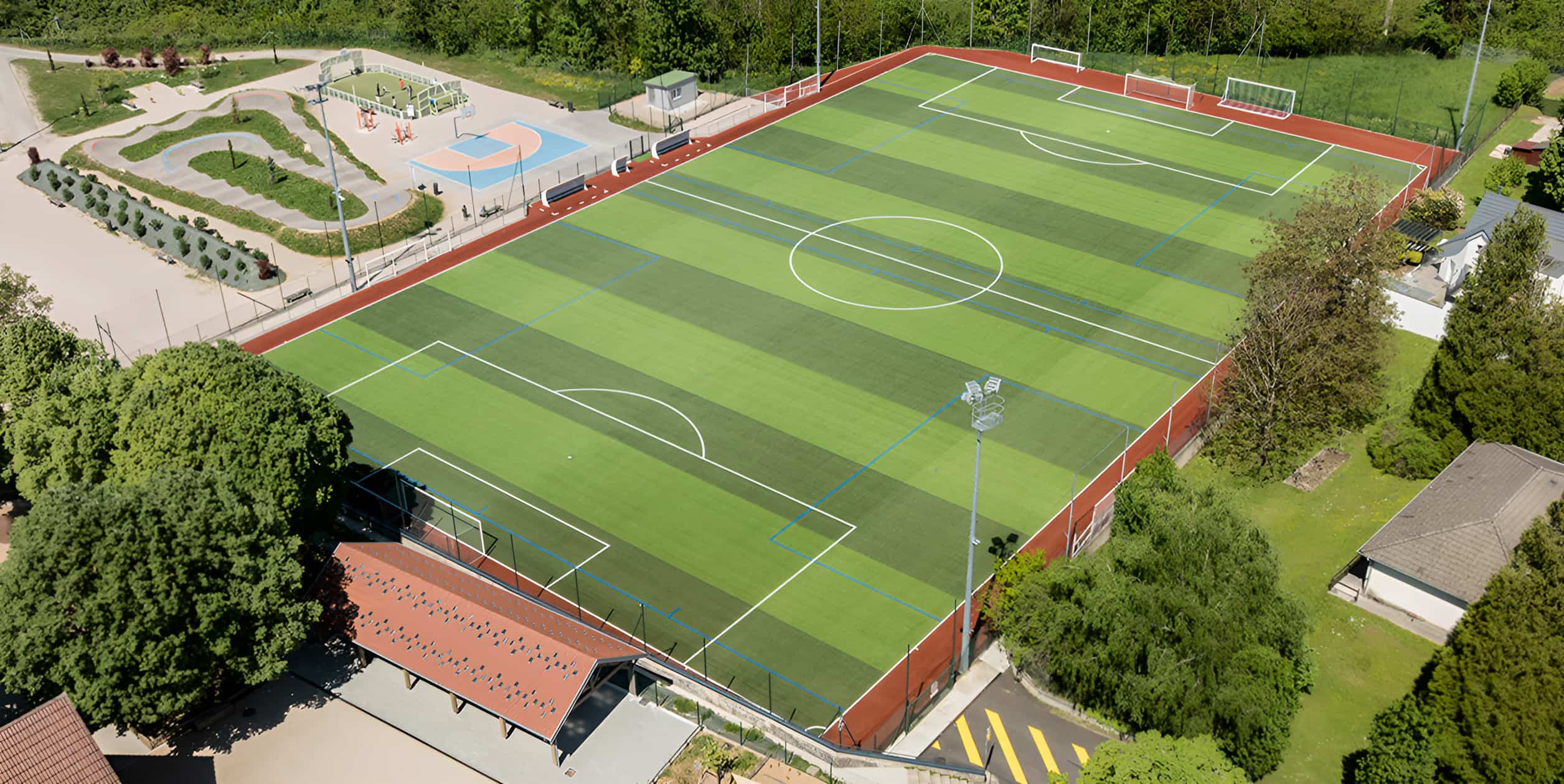 Aerial view of an artificial turf football pitch with blue and white markings, red perimeter track, and surrounding recreational facilities