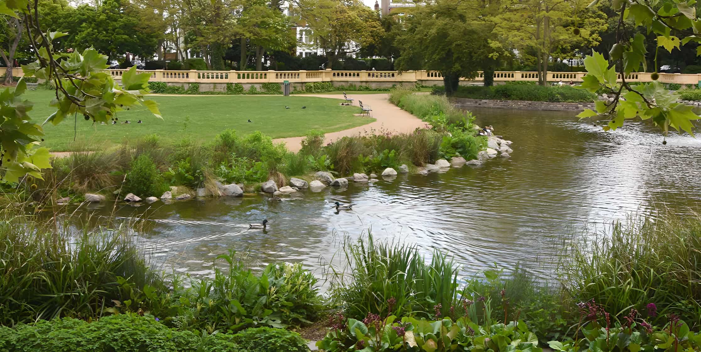 Ornamental park pond with mallard ducks, rockery planting, curved gravel path and stone balustrade boundary wall.
