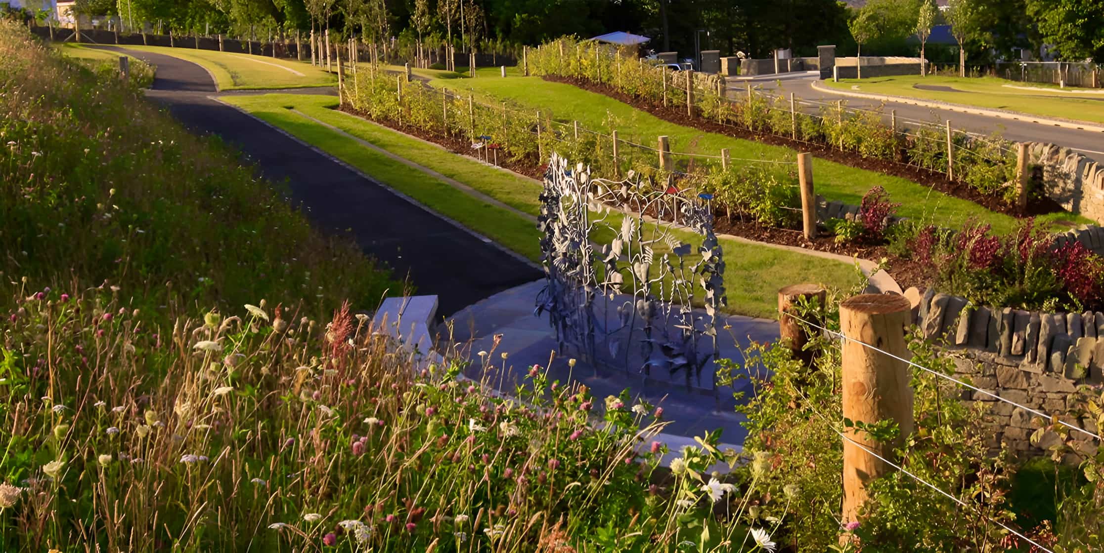 Metal botanical sculpture as garden centrepiece, surrounded by wildflowers, manicured lawns and young trees in a landscaped park