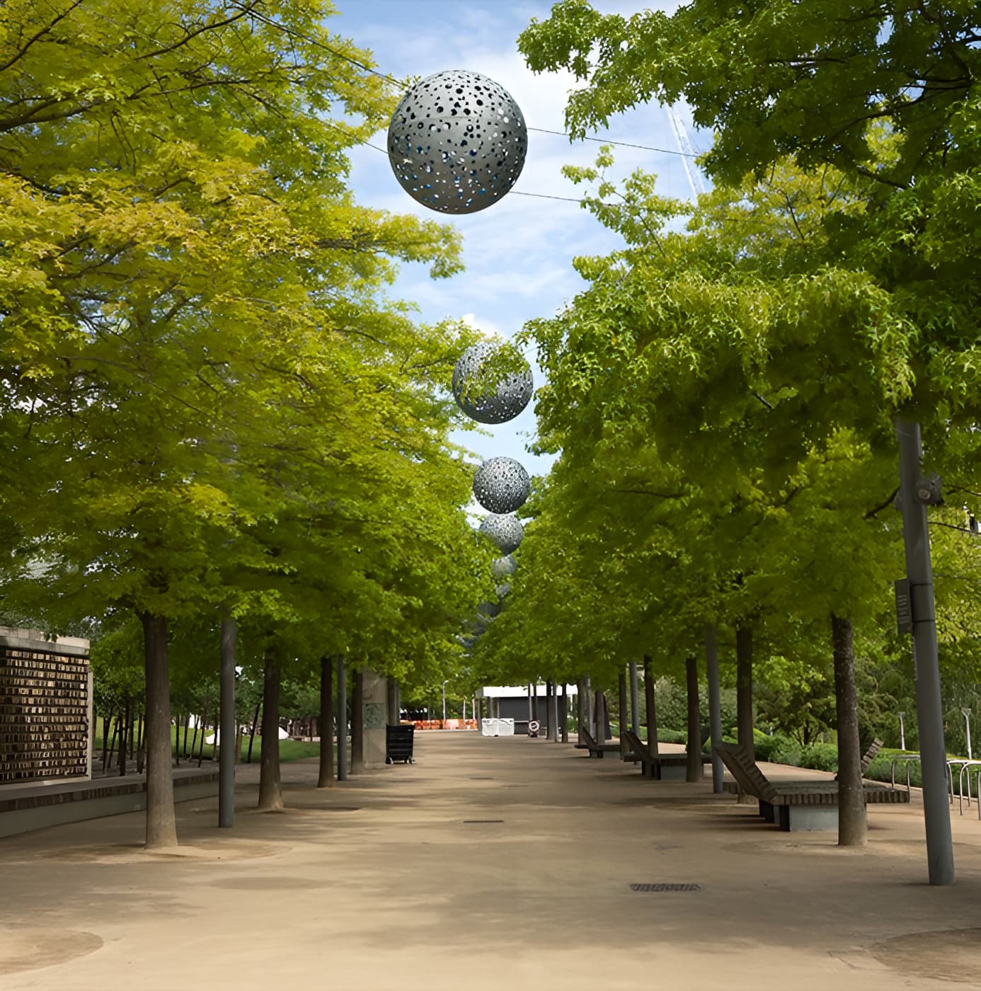 Tree-lined park pathway with suspended perforated metal sphere sculptures hanging above the walkway