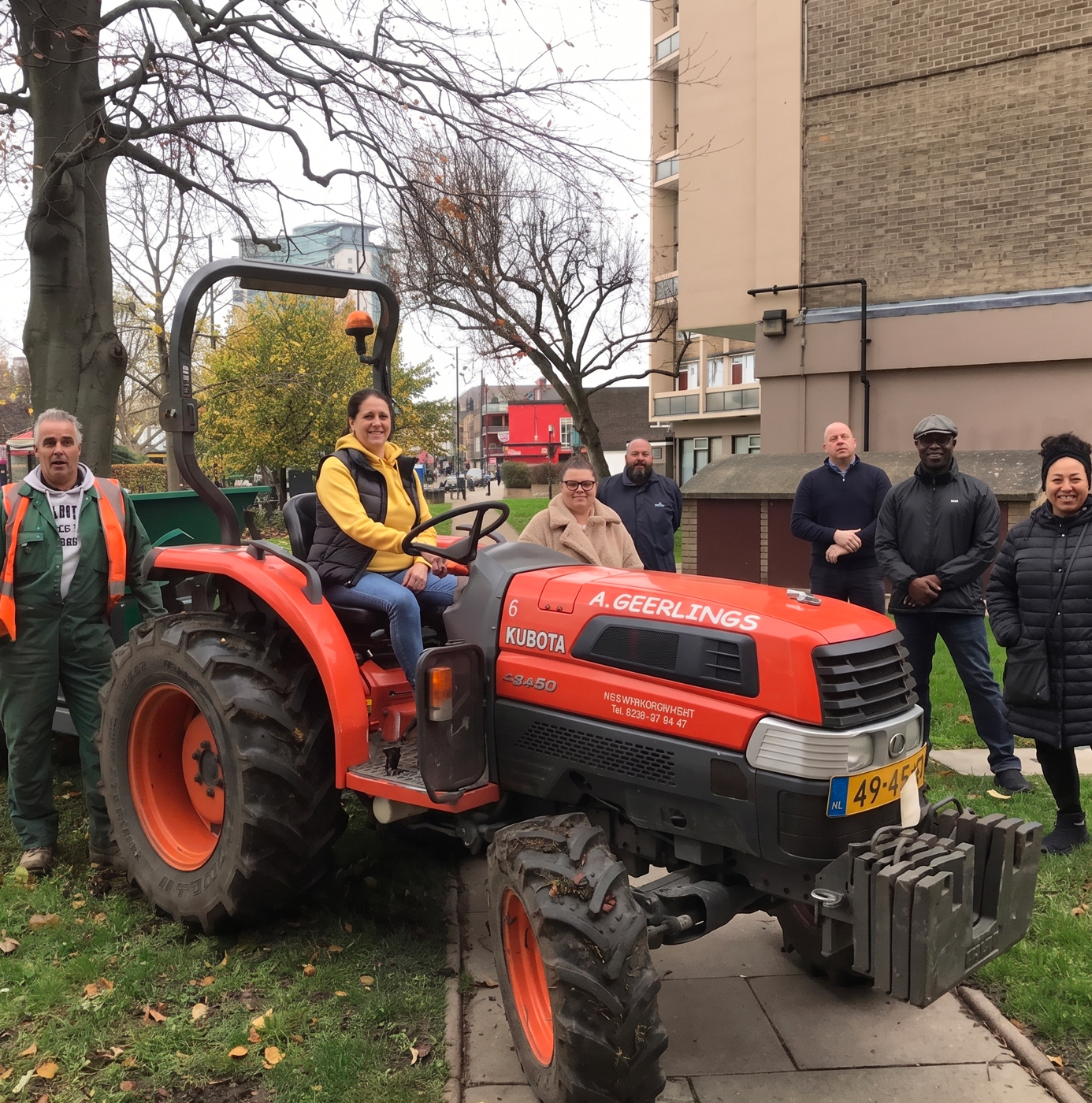 A mixed group of people posing with a Kubota tractor in an urban park setting during autumn