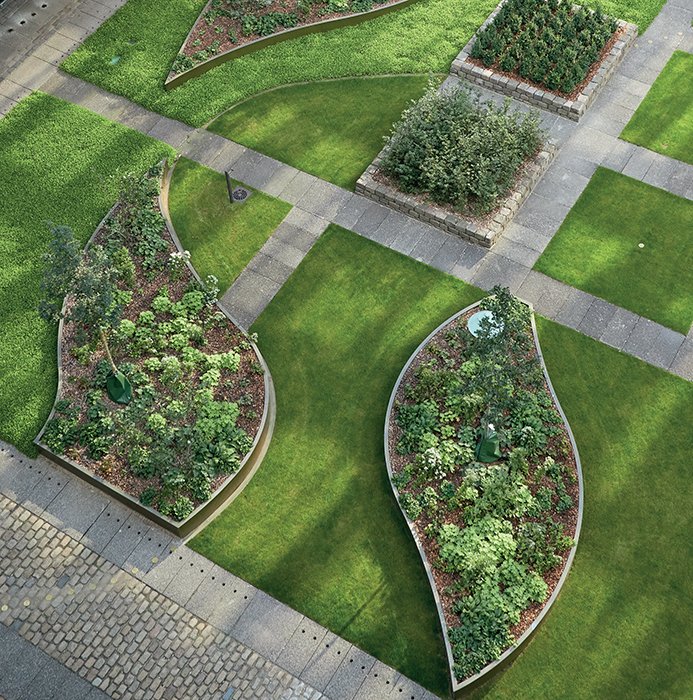 Aerial view of a formal garden with leaf-shaped raised beds, lush green lawns, and stone pathways in a geometric layout.