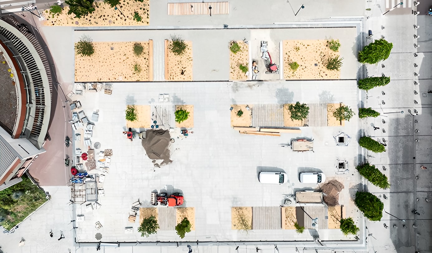 Aerial view of urban plaza landscaping installation with raised planters, trees, and construction equipment in progress