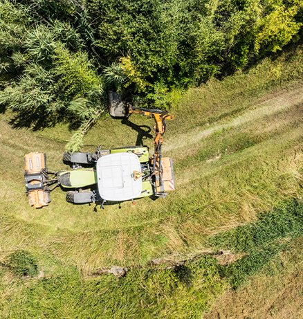 Aerial view of a CLAAS tractor with front and rear mowing attachments cutting grass on a sloped field