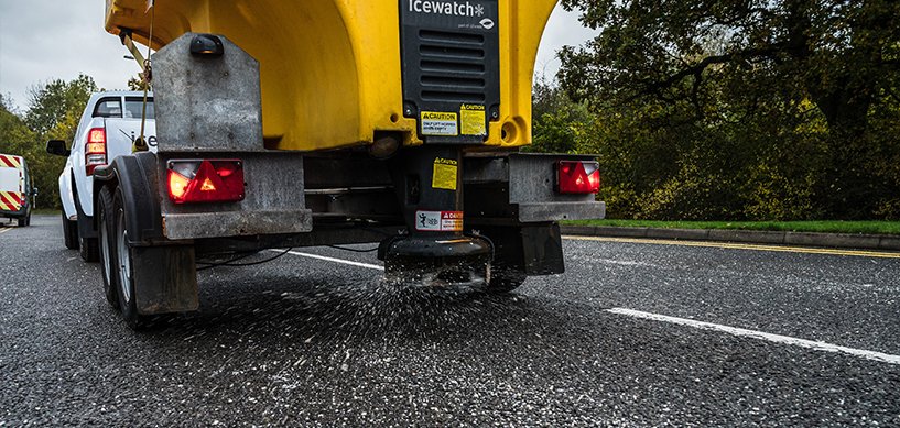 Icewatch gritter spreader unit mounted on a yellow truck spreading salt on a wet road in autumn