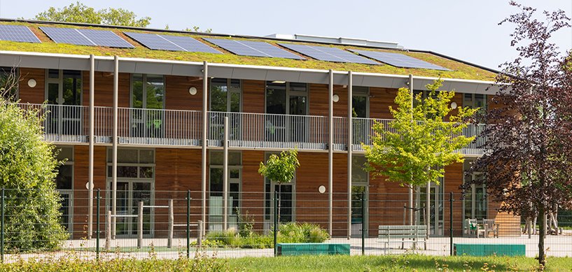 Eco-friendly two-storey building with green roof, solar panels, wooden cladding and landscaped grounds with young trees