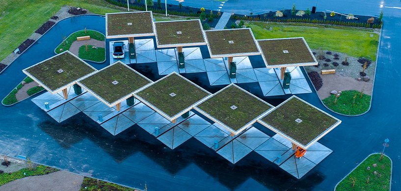 Aerial view of diamond-shaped EV charging canopies with green sedum roofs in a landscaped car park