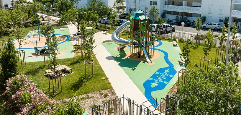 Modern playground with spiral slide tower, rubber safety surface, climbing frames, and green spaces in a residential area