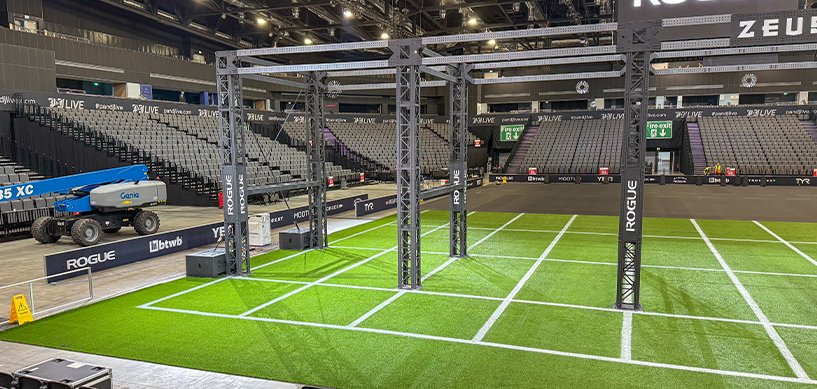 Artificial turf installed in indoor sports arena with Rogue fitness rigs and marked white lane lines on green surface