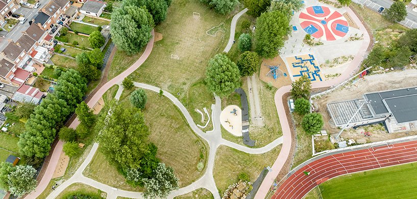 Aerial view of urban park with winding paths, playground, basketball courts, running track, and residential area