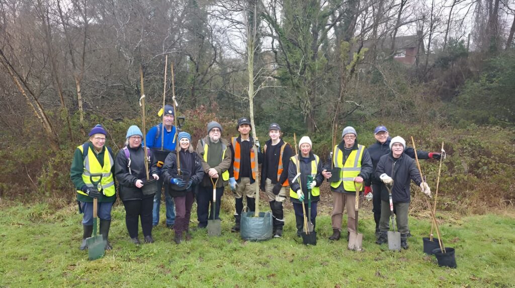 idverde volunteers in hi-vis vests planting trees with spades in a woodland area during winter