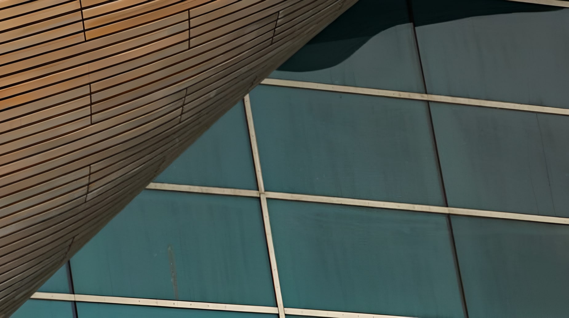 Close-up of a modern building facade contrasting warm wooden cladding with angular teal glass panel grid