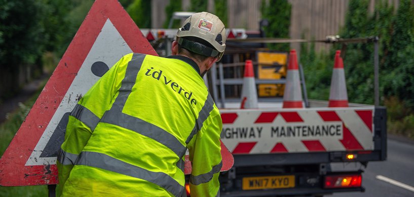 idverde worker in hi-vis jacket placing road warning sign beside highway maintenance vehicle with traffic cones