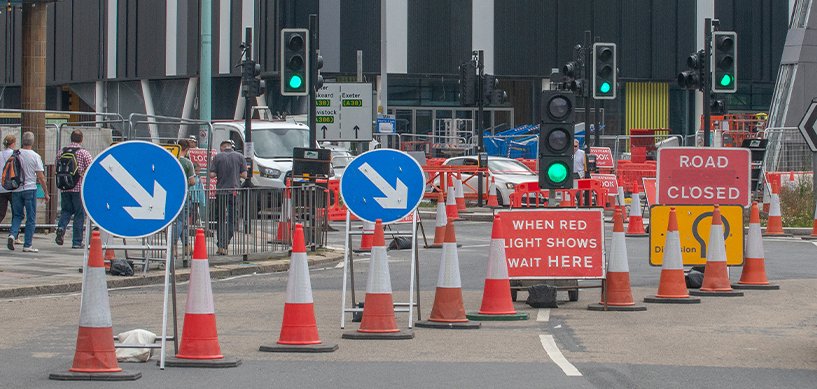 Road construction zone with traffic cones, road closed sign, and green traffic lights on a busy UK street