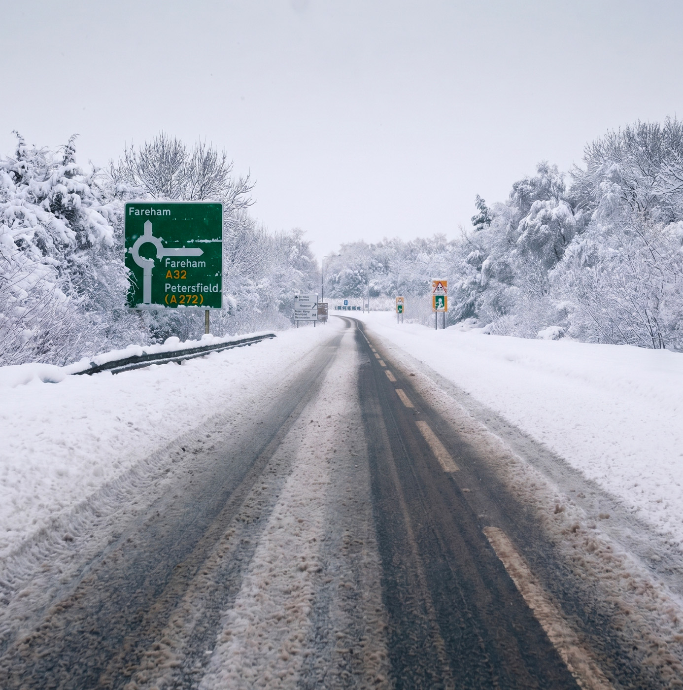 A snow-covered rural road near Fareham with heavy snowfall on trees and verges and vehicle tyre tracks visible on the carriageway.