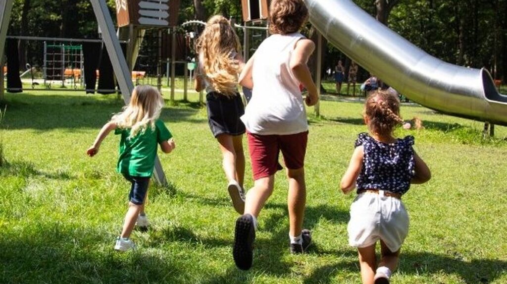 Children running across grass towards a playground slide together