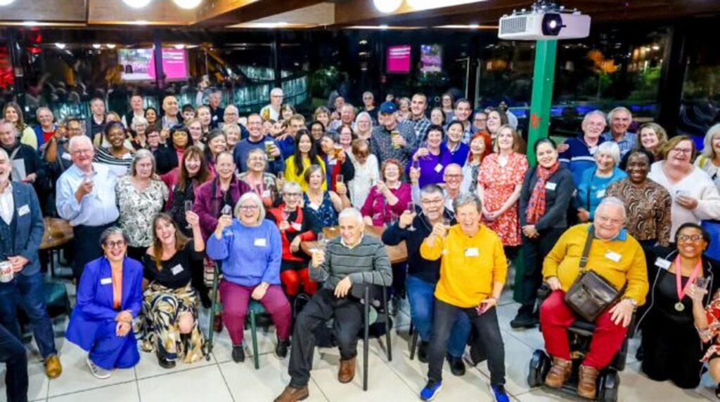 Large group of volunteers smiling and raising glasses in celebratory toast