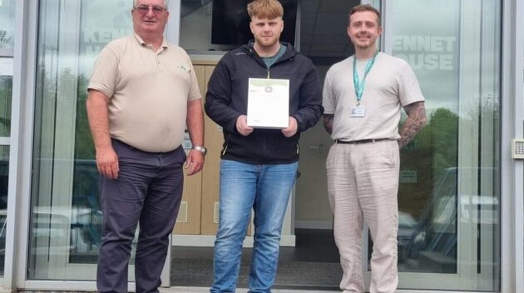 Three men standing outside Kennet House, one holding a certificate
