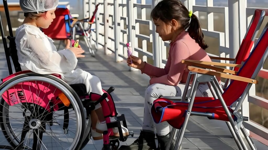 Two young girls, one in a wheelchair, playing together outdoors