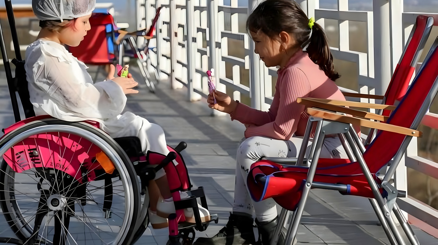 Two young girls, one in a wheelchair, playing together outdoors