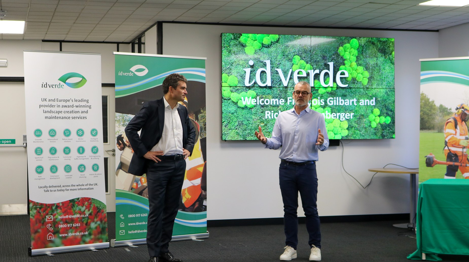 Two men presenting at idverde event with branded screen and banners
