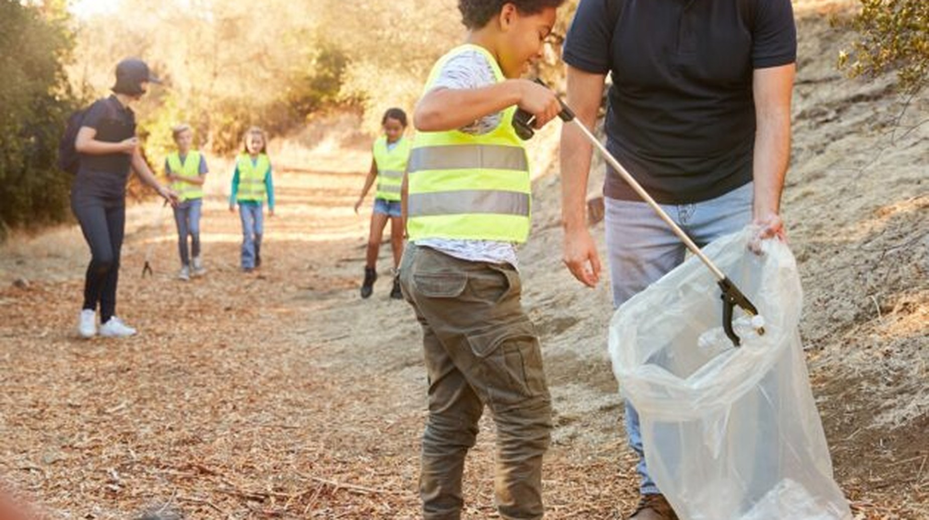 Children and adults in high-visibility vests litter picking on a woodland path