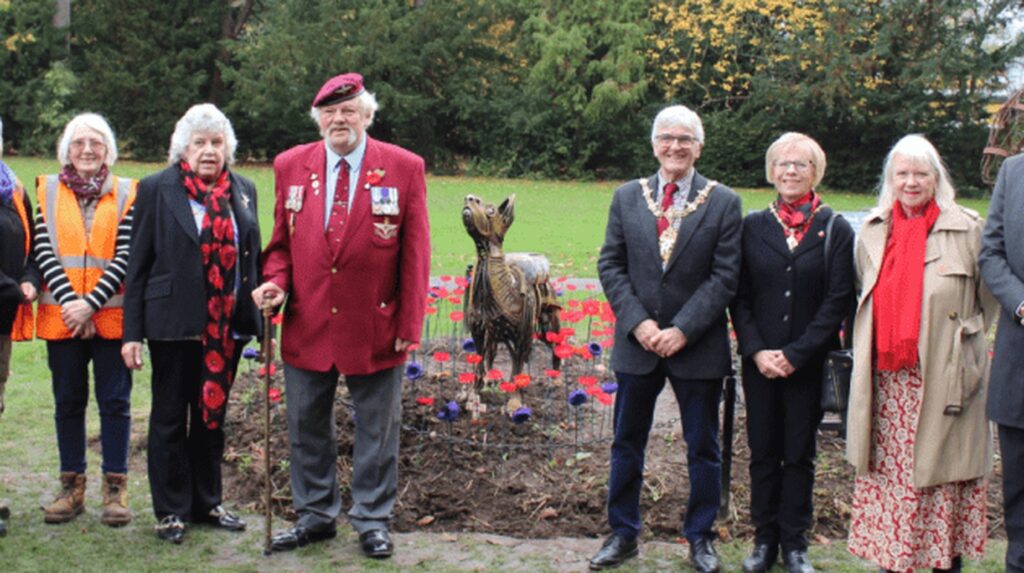 Group gathered around Bing the War Dog memorial statue with poppies