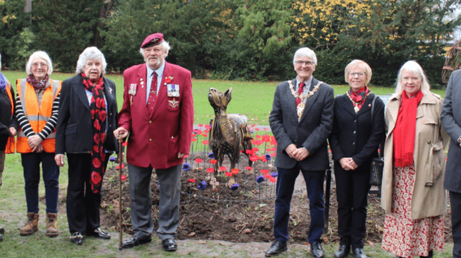Group gathered around Bing the War Dog memorial statue with poppies