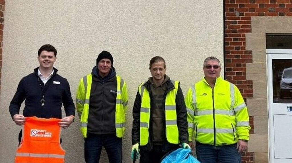 Four men in hi-vis jackets pose outside, one holding an orange safety vest