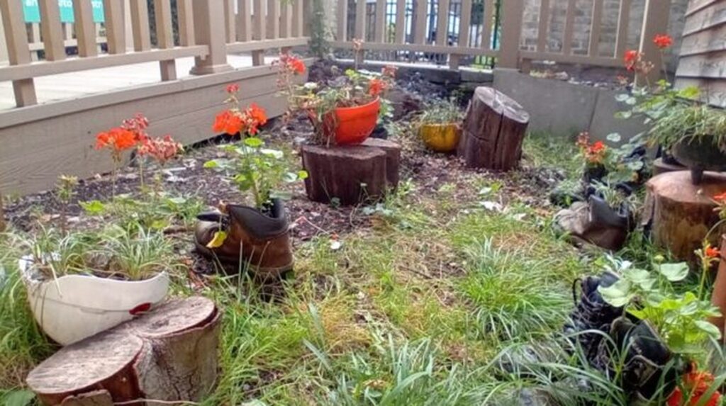 Recycled boots and log stumps used as planters in a garden bed