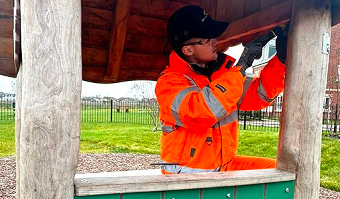 An idverde operative in high-visibility jacket carrying out a close structural inspection inside a timber play structure.