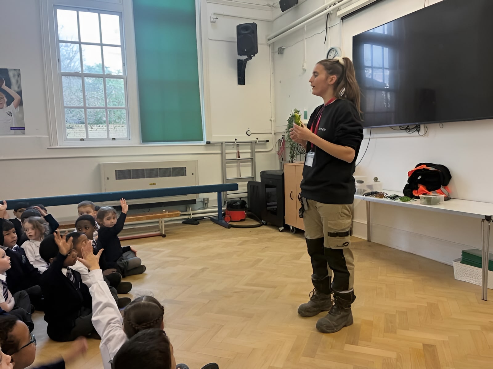idverde team member holding a frog while presenting to primary school children seated on a hall floor
