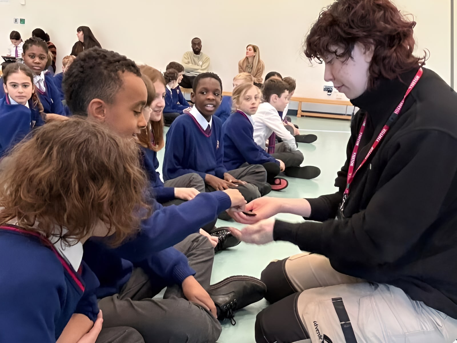 Teacher engaging with primary school students in school uniforms sitting on a classroom floor during an interactive session.