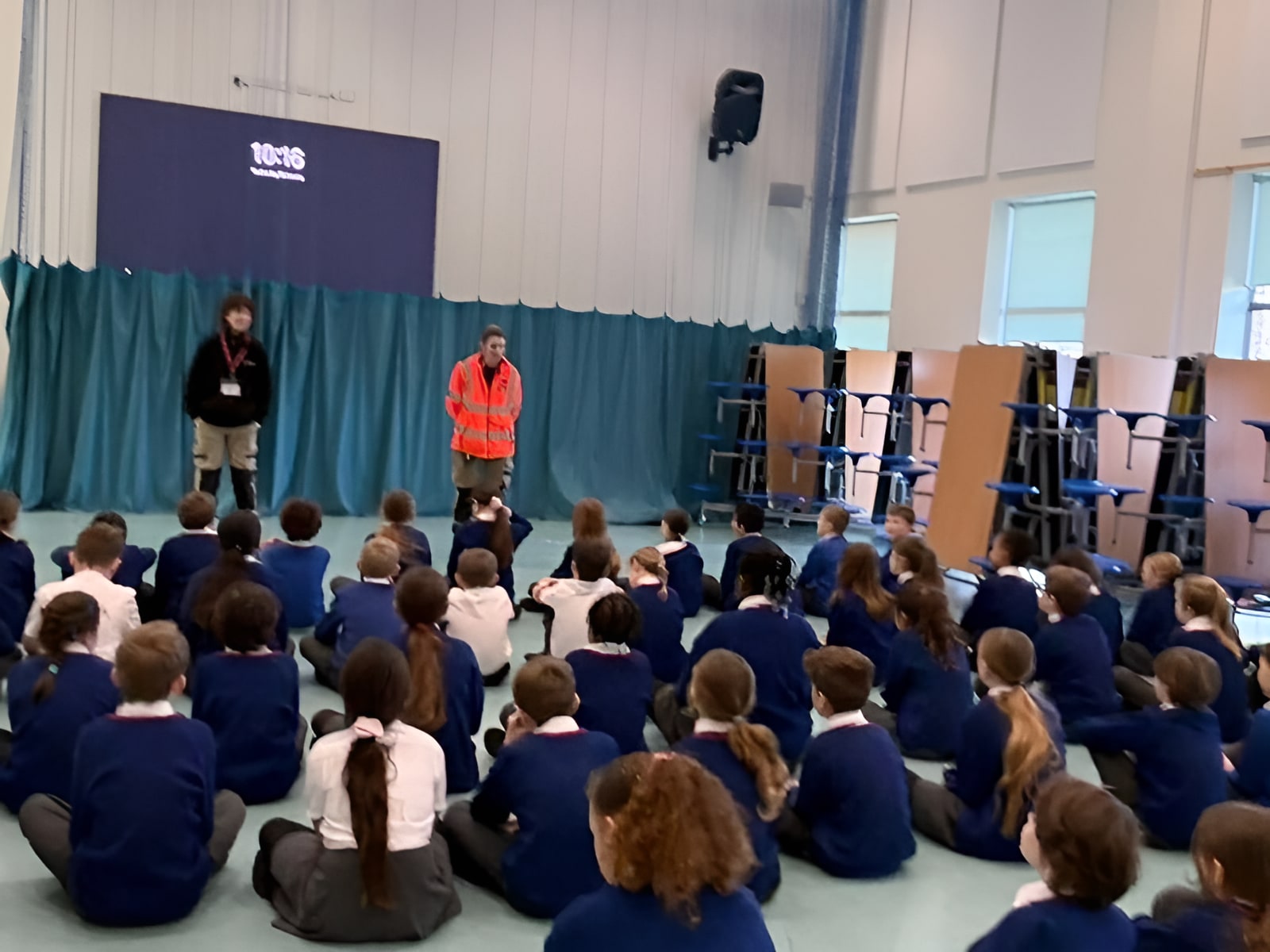idverde worker in hi-vis jacket presenting to school children seated on a gym floor during an assembly