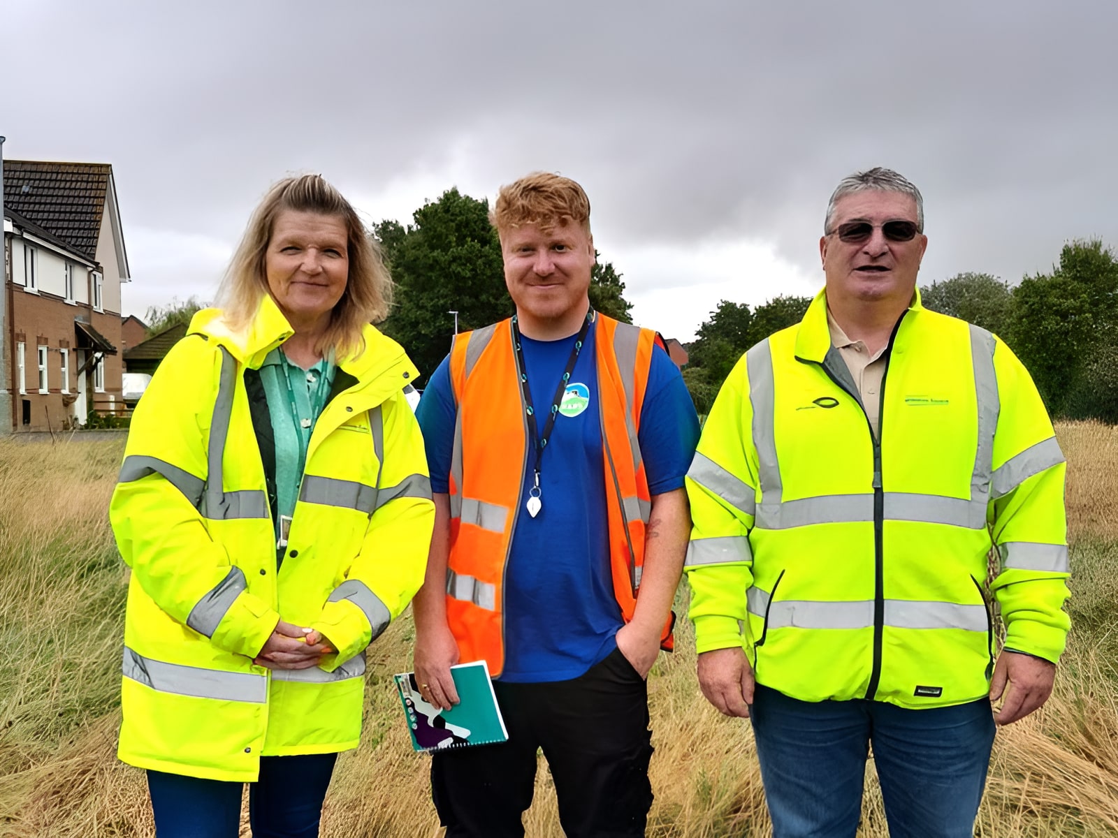 Three idverde staff in hi-vis jackets standing on a grassy site during an outdoor grounds inspection.